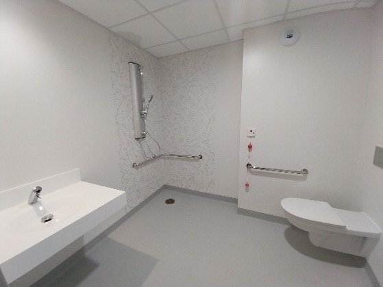 Salle d'eau accessible aux personnes à mobilité réduite, équipée de barres d'appui et d'une douche de plain-pied.