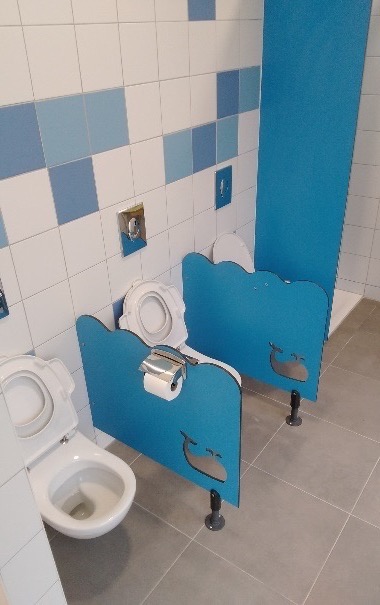 Bloc sanitaire adapté à la petite enfance avec cloisons basses et appareils à hauteur d'enfant.